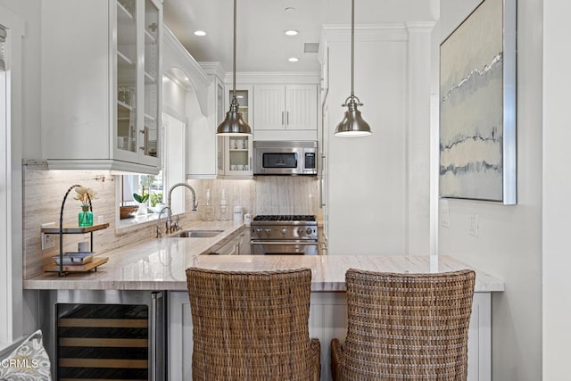 bar with sink, stainless steel appliances, white cabinets, decorative light fixtures, and beverage cooler