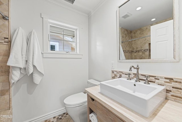 bathroom with a tile shower, backsplash, vanity, toilet, and crown molding