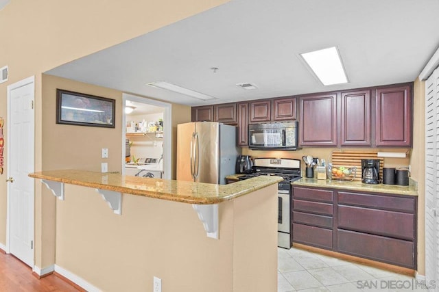 kitchen featuring light tile patterned flooring, a kitchen breakfast bar, kitchen peninsula, stainless steel appliances, and light stone countertops