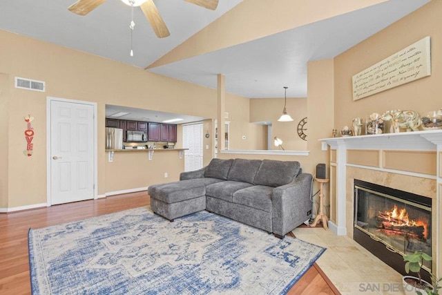 living room with lofted ceiling, a fireplace, ceiling fan, and light hardwood / wood-style flooring