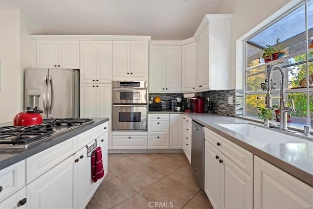 kitchen featuring sink, light tile patterned floors, stainless steel appliances, white cabinets, and decorative backsplash