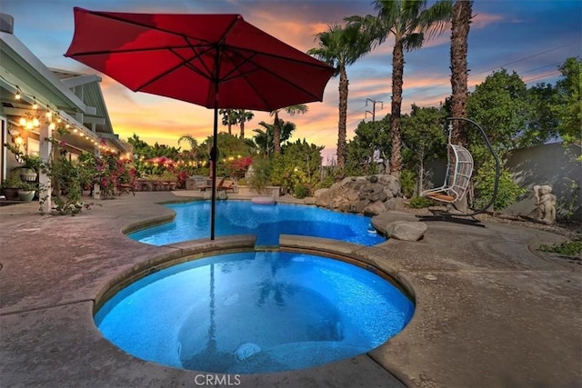 pool at dusk featuring an in ground hot tub and a patio