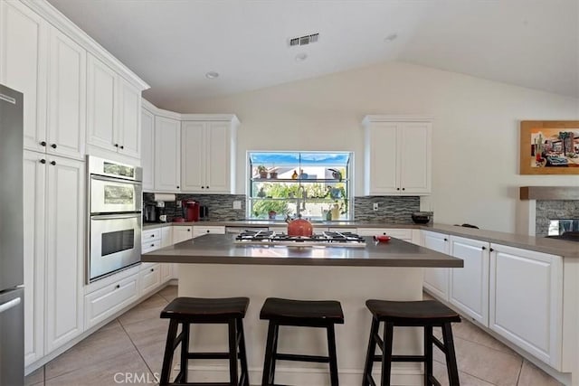 kitchen featuring appliances with stainless steel finishes, a breakfast bar, lofted ceiling, white cabinets, and backsplash