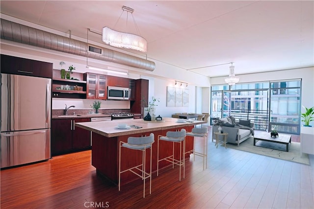 kitchen with appliances with stainless steel finishes, dark wood-type flooring, pendant lighting, and a kitchen breakfast bar