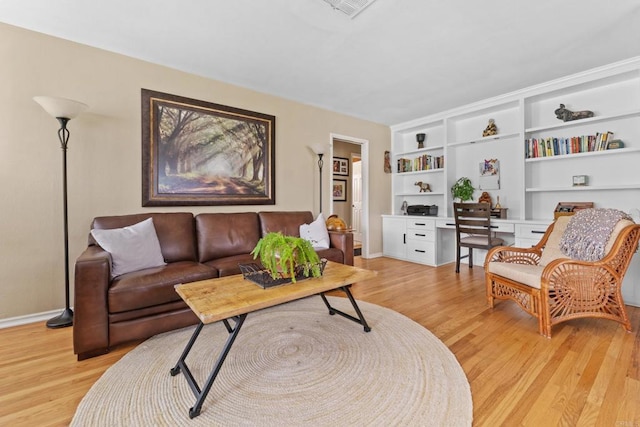 living room with built in shelves, built in desk, and light hardwood / wood-style floors