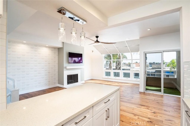 kitchen with white cabinetry, decorative light fixtures, a fireplace, and light hardwood / wood-style flooring