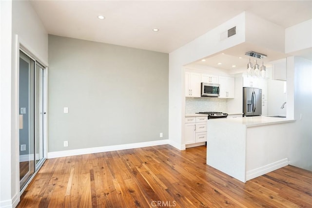 kitchen with tasteful backsplash, kitchen peninsula, stainless steel appliances, light hardwood / wood-style floors, and white cabinets