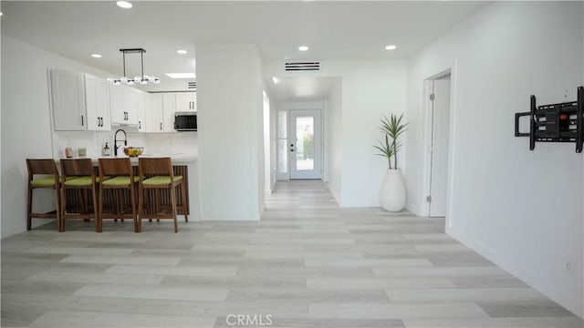 kitchen with a kitchen bar, white cabinetry, light hardwood / wood-style flooring, kitchen peninsula, and pendant lighting