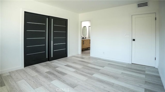 unfurnished bedroom with ensuite bath and light hardwood / wood-style flooring