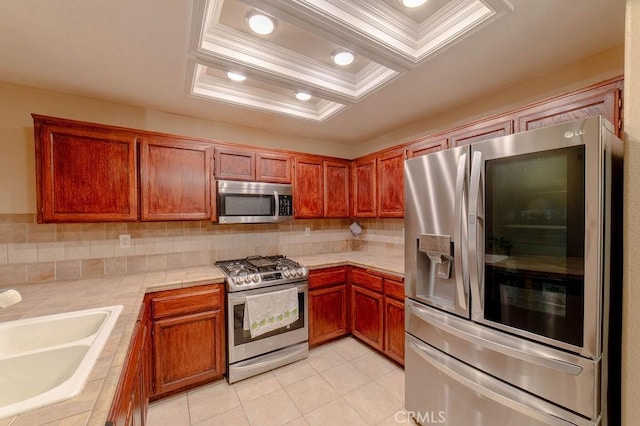 kitchen with appliances with stainless steel finishes, tile countertops, sink, a tray ceiling, and crown molding