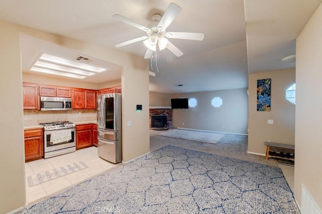 kitchen with ceiling fan, stainless steel appliances, light carpet, a brick fireplace, and decorative backsplash