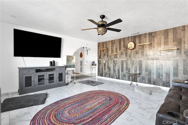 living room with ceiling fan, a textured ceiling, and wood walls