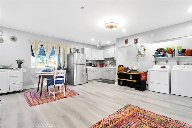 kitchen with light wood-type flooring, appliances with stainless steel finishes, white cabinets, washing machine and dryer, and backsplash