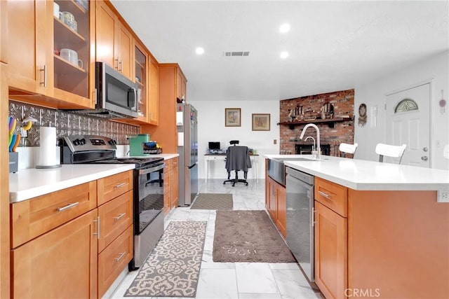 kitchen featuring stainless steel appliances, a kitchen island with sink, sink, and backsplash