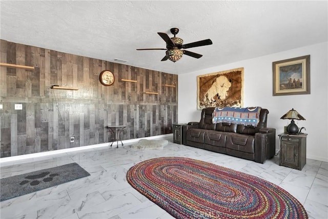 living room with ceiling fan, a textured ceiling, and wood walls