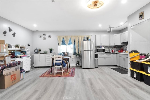 kitchen featuring stainless steel appliances, light wood-type flooring, white cabinets, and backsplash