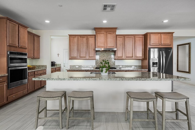 kitchen featuring light stone counters, appliances with stainless steel finishes, a breakfast bar, and a center island with sink