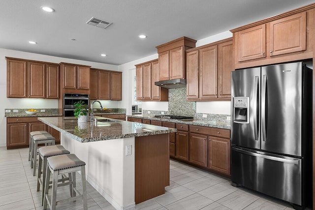 kitchen with appliances with stainless steel finishes, a breakfast bar, an island with sink, sink, and dark stone countertops