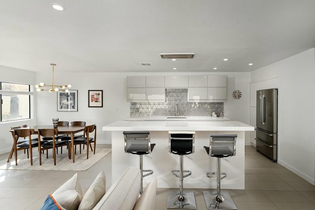 kitchen featuring light tile patterned floors, stainless steel refrigerator, white cabinetry, hanging light fixtures, and decorative backsplash