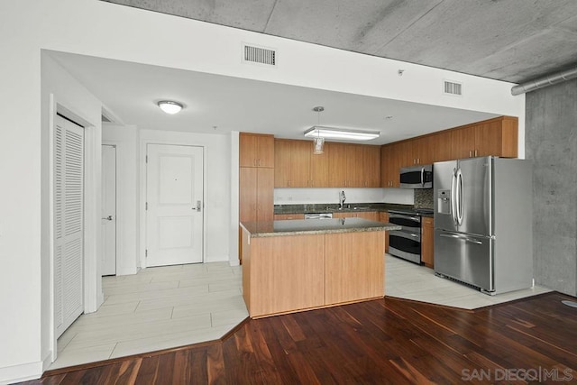 kitchen with pendant lighting, sink, stainless steel appliances, a center island, and light hardwood / wood-style floors