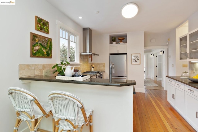 kitchen featuring stainless steel refrigerator, wall chimney exhaust hood, kitchen peninsula, and white cabinets