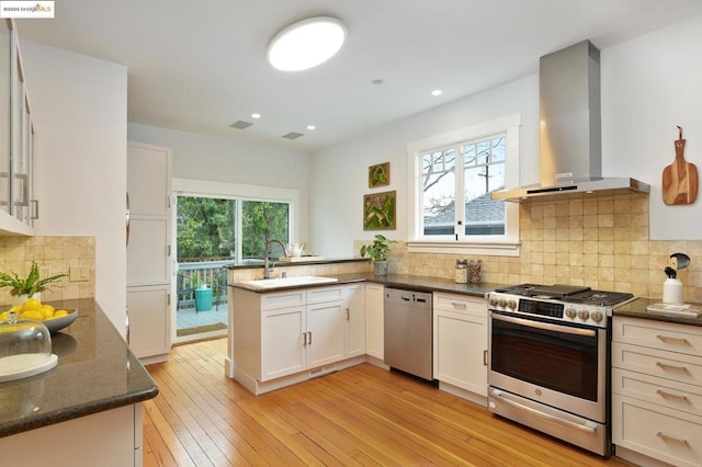 kitchen with white cabinetry, appliances with stainless steel finishes, wall chimney exhaust hood, and kitchen peninsula