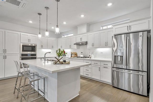 kitchen with white cabinetry, decorative light fixtures, an island with sink, and appliances with stainless steel finishes