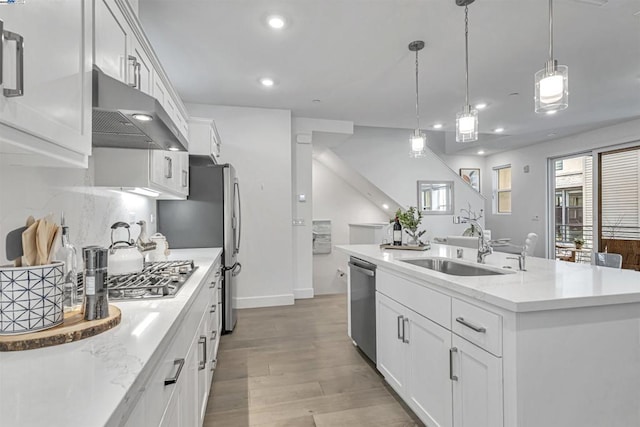 kitchen featuring sink, white cabinetry, range hood, stainless steel appliances, and an island with sink