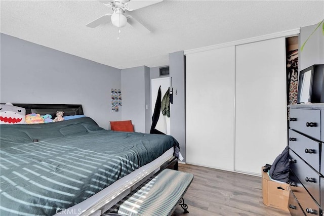 bedroom with a textured ceiling, light hardwood / wood-style flooring, a closet, and ceiling fan