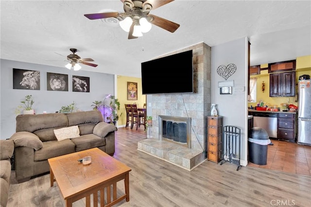 living room with ceiling fan, light hardwood / wood-style floors, a tile fireplace, and a textured ceiling