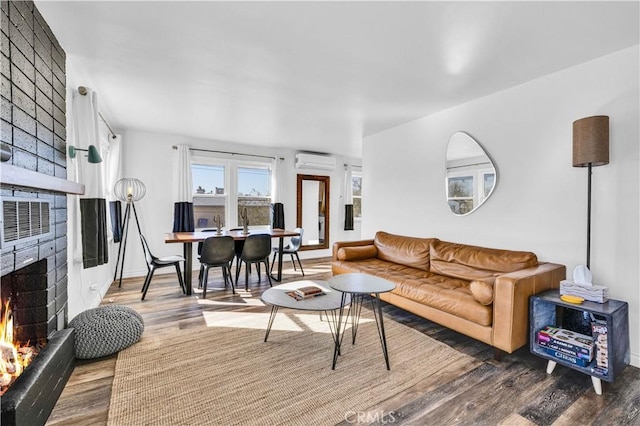 living room with a brick fireplace, hardwood / wood-style floors, and an AC wall unit