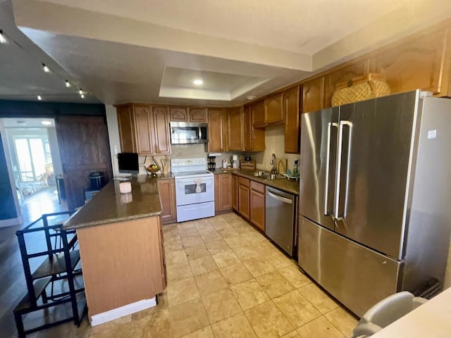 kitchen featuring appliances with stainless steel finishes, a breakfast bar, sink, dark stone countertops, and a raised ceiling