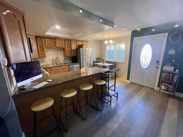 kitchen with a chandelier, a kitchen breakfast bar, a raised ceiling, hardwood / wood-style flooring, and stainless steel appliances