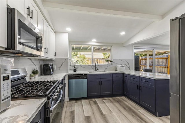 kitchen with appliances with stainless steel finishes, sink, white cabinets, light stone counters, and light hardwood / wood-style flooring