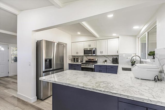 kitchen with stainless steel appliances, tasteful backsplash, light stone countertops, white cabinets, and kitchen peninsula