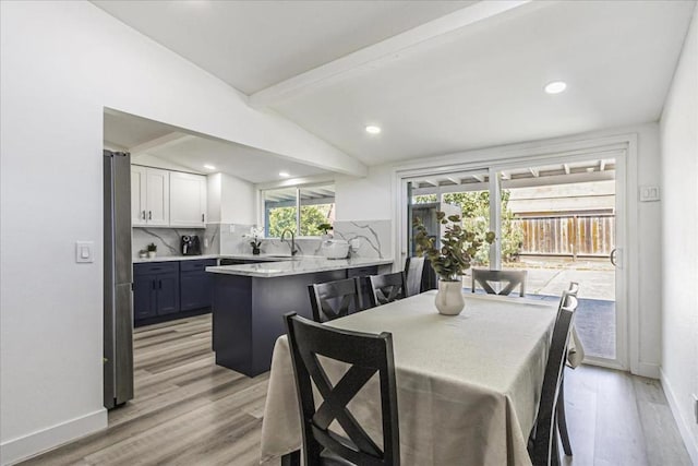 dining space with sink, vaulted ceiling with beams, and light wood-type flooring