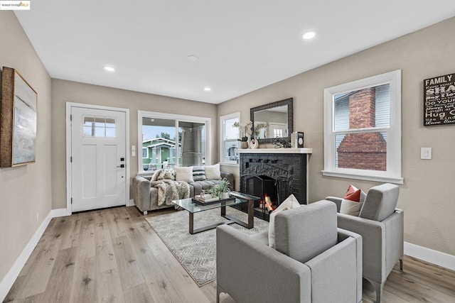 living room featuring a healthy amount of sunlight, light hardwood / wood-style floors, and a brick fireplace