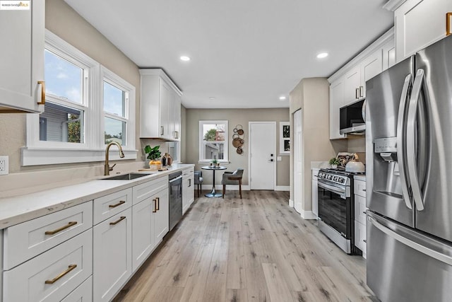 kitchen with sink, light hardwood / wood-style flooring, white cabinetry, stainless steel appliances, and light stone countertops