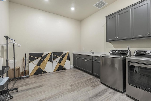 clothes washing area featuring cabinets, sink, washer and clothes dryer, and light hardwood / wood-style floors