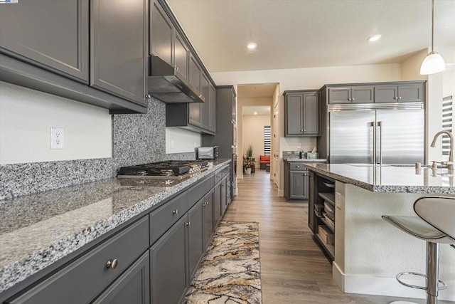 kitchen featuring dark wood-type flooring, appliances with stainless steel finishes, hanging light fixtures, light stone countertops, and decorative backsplash