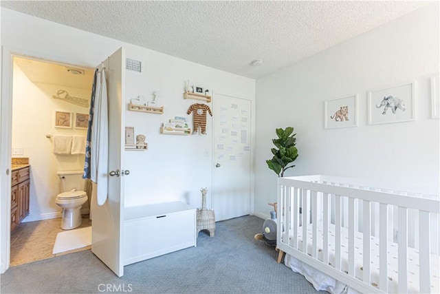 bedroom with a crib, connected bathroom, carpet, and a textured ceiling