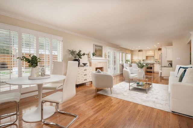 living room featuring a tile fireplace, crown molding, and light hardwood / wood-style flooring