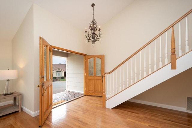 entryway with an inviting chandelier, high vaulted ceiling, and light hardwood / wood-style flooring