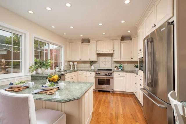 kitchen with sink, a kitchen bar, high quality appliances, tasteful backsplash, and stone countertops