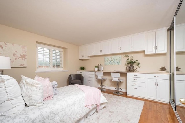 bedroom with built in desk and light hardwood / wood-style floors