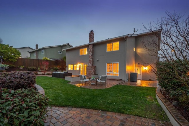 back house at dusk featuring a patio, outdoor lounge area, and a lawn