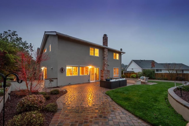 back house at dusk featuring an outdoor living space, a patio area, and a lawn