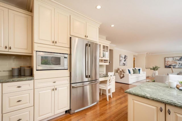 kitchen with tasteful backsplash, stainless steel appliances, crown molding, light stone countertops, and light hardwood / wood-style flooring