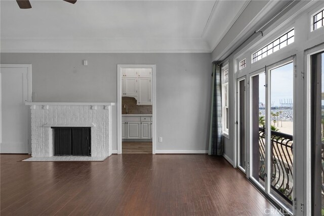 unfurnished living room featuring crown molding, dark wood-type flooring, a fireplace, and ceiling fan