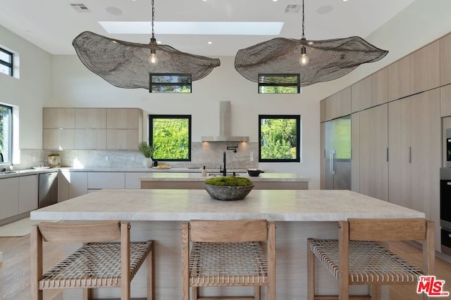 kitchen with a skylight, decorative light fixtures, a kitchen bar, and wall chimney exhaust hood